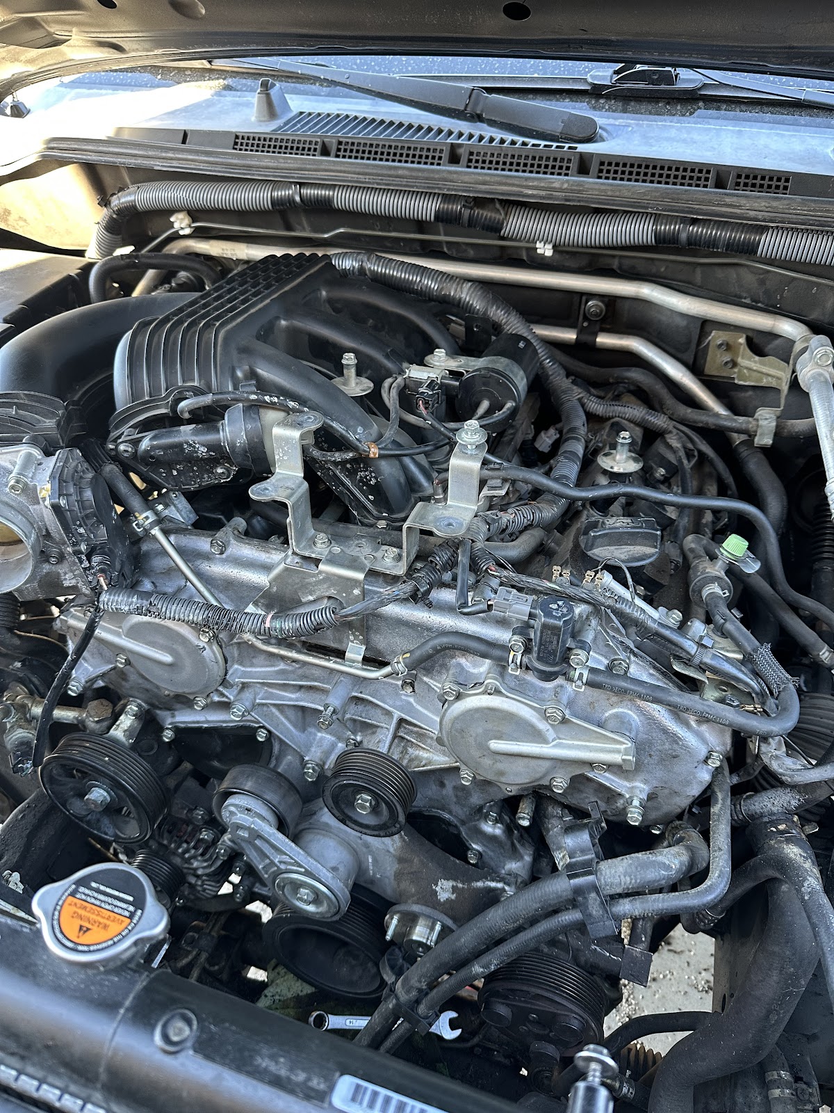 V6 engine bay opened up mid-repair with hand wrenches still sitting in the bay