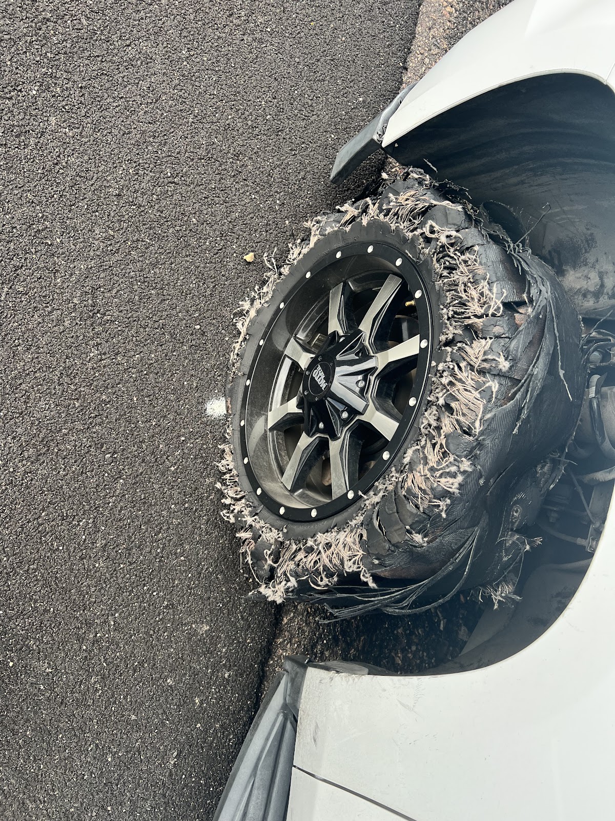 Tire shredded down to the steel belts on a lifted white truck, on the asphalt